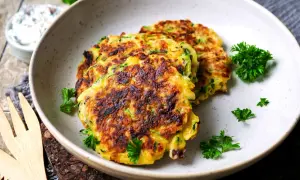 Goldbraune zucchini puffer, garniert mit Petersilie, liegen auf einem Teller. Daneben eine Schüssel mit Dip.