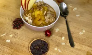 Schüssel mit Bratapfel Porridge, garniert mit Apfelscheiben und Mandelblättchen. Ein festlicher Genuss für kalte Tage.