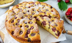 Saftiger Kirschkuchen mit frischen Kirschen, bestäubt mit Puderzucker. Ein Stück wurde bereits herausgeschnitten.