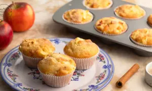 Frisch gebackene Apfelmus Muffins auf einem Teller, daneben Äpfel und Zimt.