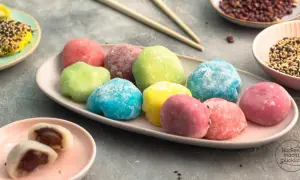Bunte Mochi-Bällchen, die Lust aufs **Mochis selber machen** machen. Auf einem Teller liegen sie in verschiedenen Farben, daneben Schüsseln mit Sesam und roten Bohnen.