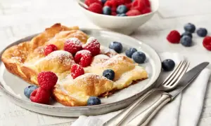 Ein goldbrauner Ofenpfannkuchen, bestäubt mit Puderzucker und garniert mit frischen Himbeeren und Blaubeeren. Perfekt für ein leckeres Ofenpfannkuchen Rezept.