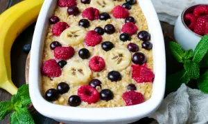 Leckere instant oats rezepte: gebackener Haferbrei mit Bananen, Himbeeren und Blaubeeren, garniert mit frischer Minze.