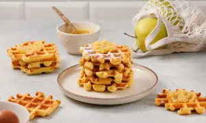 Gestapelte Waffeln mit Apfelmus bestreut, daneben ein Apfel im Netzbeutel und eine Schüssel mit Apfelmus.