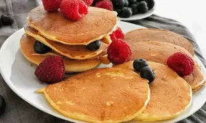 Gestapelte, goldbraune, gesunde Pancakes mit frischen Himbeeren und Blaubeeren garniert. Ein köstlicher Start in den Tag.