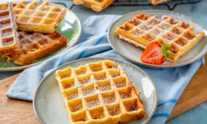 Goldbraune Waffeln, bestäubt mit Puderzucker, warten auf ein leckeres Waffeln Rezept. Eine Erdbeere garniert eine Waffel.
