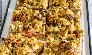 Saftiger low carb rhabarberkuchen mit knuspriger Streuselhaube und Pekannüssen, in rechteckige Stücke geschnitten.