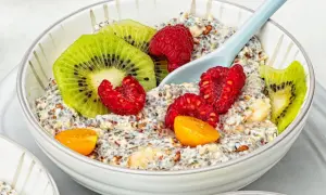 Schüssel mit Overnight Oats, garniert mit Kiwi, Himbeeren und Physalis. Ein Löffel liegt darin.