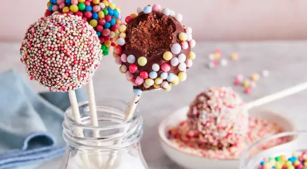Bunte cake pops, verziert mit Zuckerstreuseln, warten darauf, vernascht zu werden. Einer ist angeknabbert und zeigt den schokoladigen Kern.