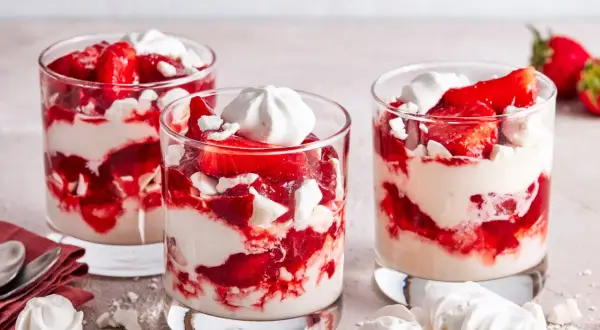 Drei Gläser mit Eton Mess: geschichtete Erdbeeren, Sahne und zerbrochene Baiser-Stücke. Ein süßer Genuss!