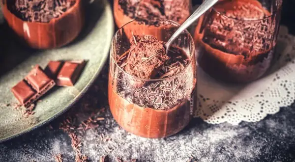 Schokoladenmousse in Gläsern, bestreut mit Schokostreuseln. Ein Löffel nimmt eine Portion auf. Perfekt für ein rezept mousse au chocolat ohne ei.