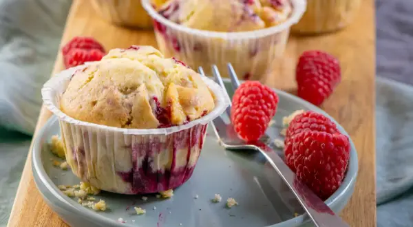 Saftige Himbeer Muffins auf einem Teller, garniert mit frischen Himbeeren. Ein Genuss für jeden Kaffeetisch.