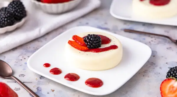 Cremige Panna Cotta, einfach im Thermomix zubereitet, garniert mit frischen Beeren und Erdbeersauce.