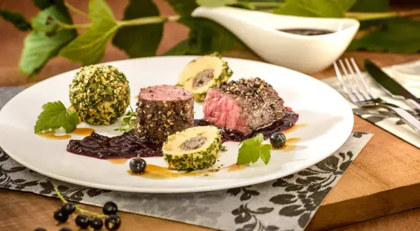 Edles Fleisch mit Kräuterkugeln und einer dunklen Sauce, inspiriert von schwarzen johannisbeere rezepten.