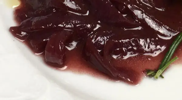 Portwein zwiebeln in einer glänzenden, dunklen Sauce auf einem weißen Teller, garniert mit Rosmarin.
