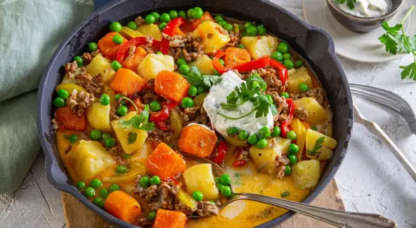 Herzhafte Hackfleischpfanne mit Kartoffeln, Karotten und Erbsen. Eine tolle Idee für ein schnelles Abendessen, garniert mit frischer Petersilie und einem Klecks Sour Cream.