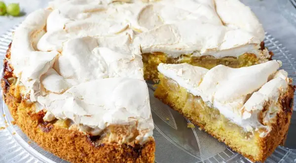 Omas stachelbeerkuchen mit luftiger Baiserhaube auf einem Tortenteller. Ein Stück ist bereits angeschnitten.