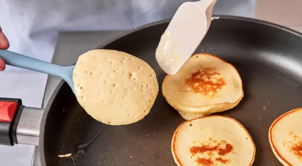 Pancakes rezept mit joghurt: goldbraune Pfannkuchen werden in einer Pfanne gebacken, ein Löffel Teig wird hinzugefügt.
