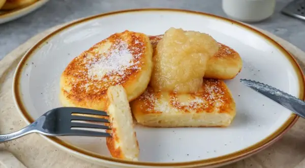 Goldbraune Quarkkeulchen, bestreut mit Puderzucker, serviert mit Apfelmus. Ein köstliches Quarkkeulchen Rezept zum Genießen.