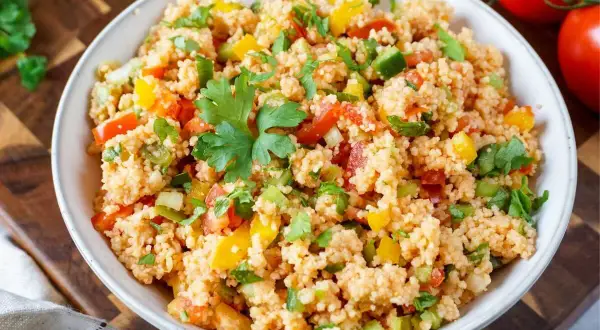 Bunter Couscous-Salat mit Tomaten, Paprika und frischer Petersilie, garniert mit einem Petersilienblatt.