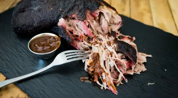 Saftiges Pulled Pork, perfekt für ein gerupftes Rezept. Eine Gabel nimmt zarte Fleischfasern auf, daneben eine Schale BBQ-Sauce.