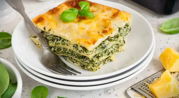 Ein Stück Spinatlasagne mit Käse überbacken, garniert mit Basilikum. Ein köstliches spinatlasagne rezept.