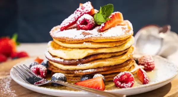 Ein Stapel amerikanischer Pancakes, bestäubt mit Puderzucker und garniert mit frischen Beeren und Minze.
