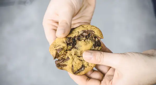 Hände halten einen zerbrochenen schoko cookie mit geschmolzener Schokolade.