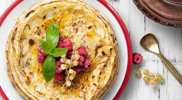 Gestapelte Pfannkuchen ohne Mehl, beträufelt mit Honig und garniert mit frischen Beeren und Minze. Ein köstlicher Genuss!