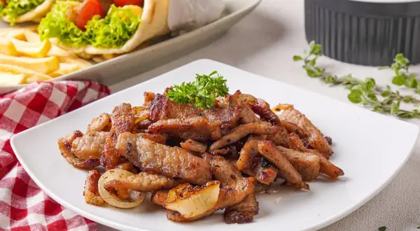Saftiges Fleisch für ein köstliches Gyros Rezept, garniert mit Petersilie. Daneben liegen Gyros-Wraps und ein Gurkensalat.