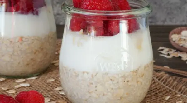Zwei Gläser mit overnight oats mit joghurt und frischen Himbeeren. Ein gesunder Start in den Tag.