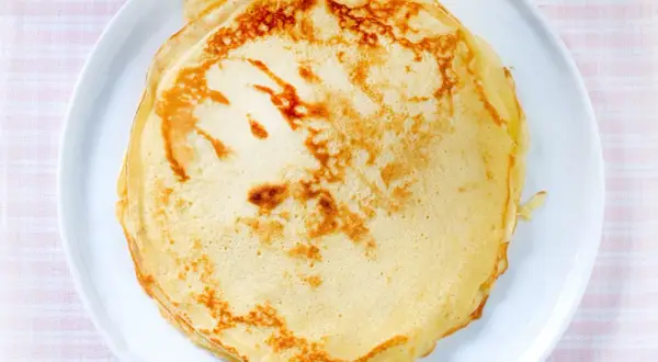 Ein Stapel goldbrauner, veganer Pfannkuchen liegt auf einem weißen Teller. Perfekt für ein leichtes Frühstück.