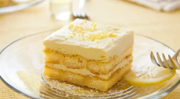 Ein Stück Limoncello Tiramisu auf einem Teller, garniert mit Zitronenschale. Ein Hauch von Sommer auf jedem Löffel.