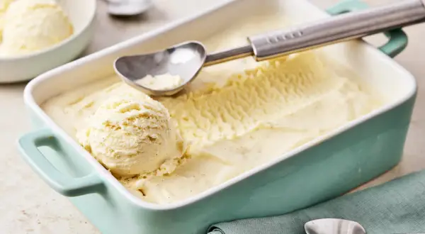 Ein Behälter mit cremigem Vanilleeis, perfekt zum vanilleeis selber machen. Ein Löffel liegt bereit, um die erste Kugel zu entnehmen.