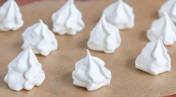 Weiße Baiser-Häufchen, bereit für das Baiser Rezept. Sie liegen auf Backpapier und sehen luftig und leicht aus.