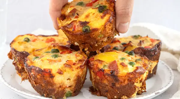 Goldbraune, herzhafte Pizza Muffins mit bunten Gemüsestückchen und Käse, die gerade aus dem Ofen kommen.