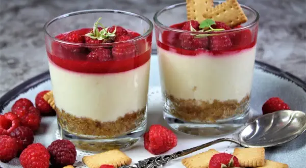 Zwei Gläser mit cremigen Desserts, garniert mit Himbeeren und Keksen. Perfekt für Ihre nächsten Dessert Rezepte.
