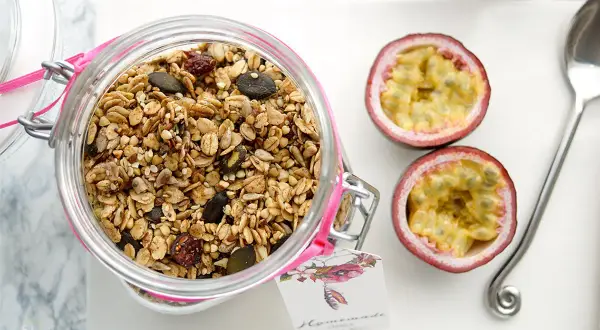 Glas mit selbstgemachtem Granola, Kürbiskernen und Trockenfrüchten. Daneben zwei Passionsfrüchte und ein Löffel.