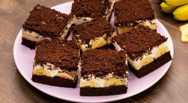 Saftiger Maulwurfkuchen vom Blech mit Bananen und Schokostreuseln auf einem rosa Teller.