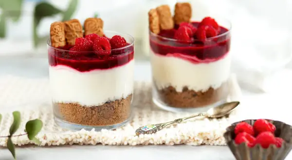 Zwei Gläser mit einem köstlichen, warmer nachtisch: Kekskrümel, cremige Schicht, Himbeersoße und frische Beeren.