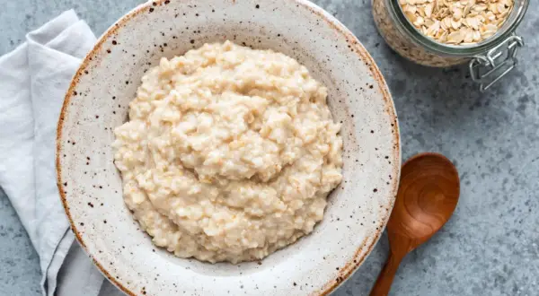 Cremiger Haferbrei in einer Schale, daneben ein Glas Haferflocken. Ein einfaches Porridge Rezept für einen gesunden Start.