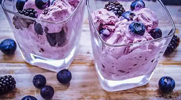 Zwei Gläser mit cremigem, lila gefärbtem frozen joghurt, garniert mit frischen Blaubeeren und Brombeeren.