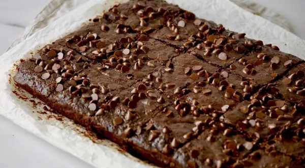 Saftige Zucchini-Brownies, bestreut mit Schokoladenstückchen, auf Backpapier.