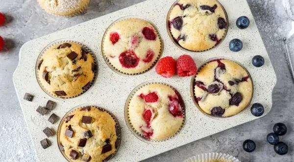 Leckeres mini muffins rezept: Schoko-, Himbeer- und Blaubeermuffins in einer Muffinform, garniert mit frischen Beeren und Puderzucker.