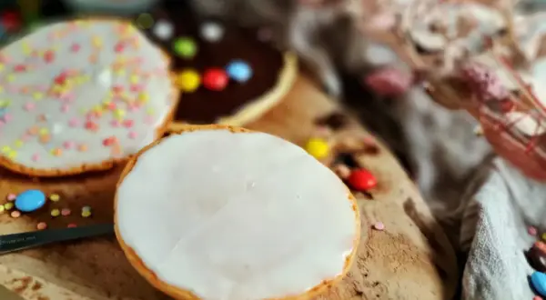 Bunte Kekse mit Zuckerguss und Schokoladenglasur, inspiriert von einem amerikanischen Rezept, liegen auf einem Holzbrett.