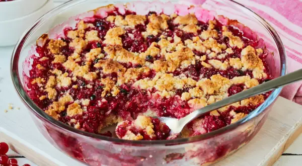 Ein leckerer Johannisbeer Crumble in einer Glasform, mit knuspriger Streuselhaube und saftiger roter Füllung.