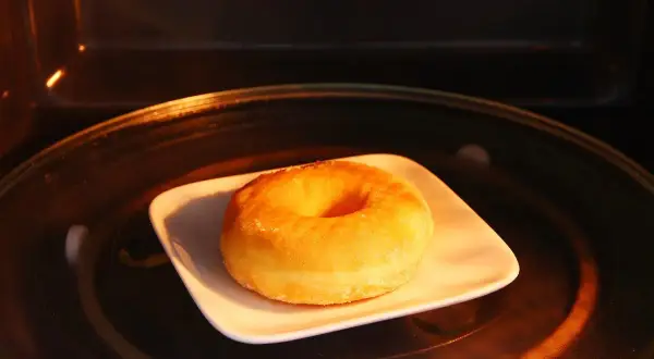 Ein einzelner Donut auf einem weißen Teller in einem Mikrowellenofen. So bleiben Donuts frisch.
