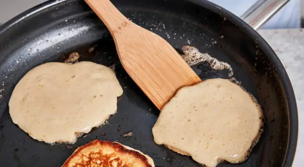 Buttermilch pancakes bräunen in der Pfanne, eine Holzspachtel wendet sie.