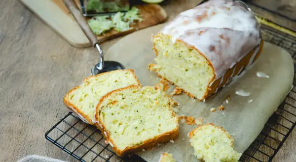 Saftiger Zucchini Kuchen mit Zuckerguss, frisch angeschnitten auf einem Gitter. Daneben liegen geriebene Zucchini und ein Hobel.