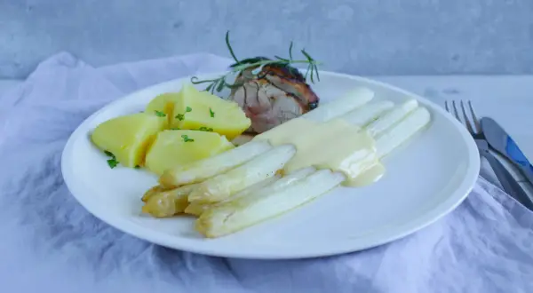Weißer Spargel mit Sauce Hollandaise, Kartoffeln und Fleisch auf einem Teller.